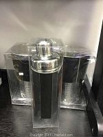 Two silver-tone hammered ice buckets and one silver-tone cocktail shake mixer in transparent open boxes.