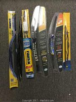 Photo of seven single windshield wiper blades in open box packaging laid out on a carpeted surface.