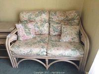 Front view of the rattan loveseat showing floral cushions and two throw pillows