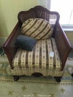 Front view of armchair showing carved wooden frame, cane back and patterned seat and back cushions with a small blue-gray pillow.