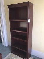 Front view of the tall brown bookcase showing five shelves and flat top.