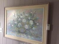 Framed oil painting hanging on a wall showing the floral artwork with pastel colors and textured brush strokes.