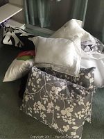 Photo showing various pillows including white pillows with lace trim and gray floral pillow shams arranged on carpet.