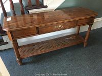 Front view of oak veneer hall table showing rectangular top, single drawer with brass handle, and cane lower shelf.