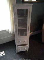 Front view of the white utility cabinet with glass door on top and two drawers below.