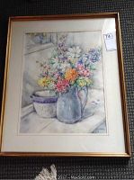 Framed watercolour painting of colorful flower arrangement with blue jug on table.