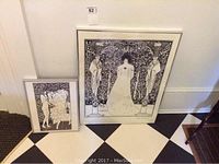 Two framed Aubrey Beardsley prints side by side on the floor, showing relative size and framing.