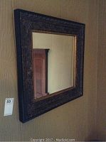 Image showing entire square wall mirror hanging on wall, reflecting door and wall in background.