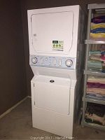 Full view of white stacked washer and dryer unit with surrounding shelving