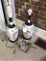 Pair of ceramic floral lamps shown side by side with their cords and two brass bird wall hooks placed in front of them on carpet.