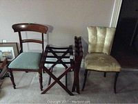 Two wooden chairs with green upholstery, two foldable wooden luggage racks, and one upholstered occasional chair with visible worn sea foam fabric seat.
