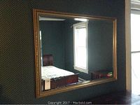 Overall front view of the rectangular framed mirror hanging on a wall, showing clarity of the reflective surface and details of the gold-toned frame.