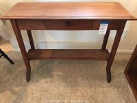 Front view of the console table showing its shaker style legs, single central drawer with square wooden pull, and lower shelf.