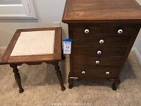 Photo showing the wood chest of drawers with six drawers and white knobs next to the antique side table with tile inset top.