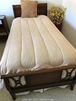 Twin bed made of medium brown wood, showing headboard and footboard with carved details, mattress covered with beige quilted fabric and beige pillow on top