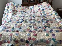 Full view of handmade quilt with interconnected ring patchwork design spread over a bed.