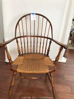 Front view of antique wooden armchair with curved spindle back and woven seat