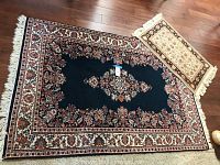4x6 navy blue rug with central floral medallion and red cream borders next to 2x4 cream and black floral rug with fringed edges on wooden floor.