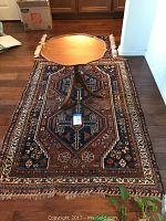 3.5'x5' navy and burnt orange geometric medallion oriental rug displayed with pedestal table on top.