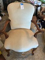 Front view of the beige custom upholstered antique armchair showing curved arms and legs.