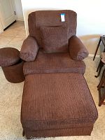 Full view of brown upholstered armchair with round and rectangular ottomans placed in front and beside the chair.