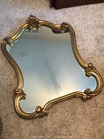 Front view of the antique gold wooden framed mirror resting on carpet, showing curved shape and reflective glass.