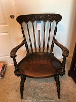 Front view of antique wooden arm chair showing carved backrest, spindles, armrests and seat.