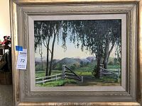 Frontal view of the oil painting showing a rural scene with gate, trees, and mountains, in a wide gold-tone frame.