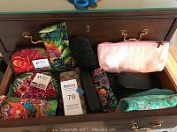 Photo of assorted women's glasses cases and coin purses inside a drawer, showing multiple colorful and patterned fabric pouches and two black eyeglass cases.