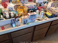 Counter filled with an assortment of personal care and health products including boxed perfumes, thermometers, and blood pressure meter.
