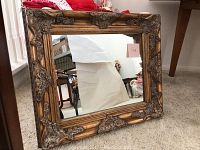 Full view of the rectangular wall mirror showing ornate gold-toned frame and reflective glass surface.