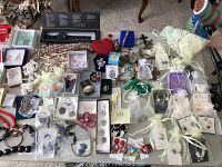 Photo showing overall view of assorted new costume jewelry spread on a table, many in boxes and organza bags.