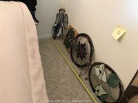 Photo showing five stained glass panels lined up, including one angel figure with trumpet and four floral oval panels with a measuring tape on the floor for scale.