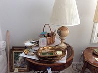 Overall lot on side table showing marble lamp, gold trays, framed poem, decorative cross, playing card basket, and coasters.