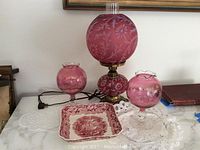 Photo showing the vintage pink glass lamp, the square Ironstone platter, two pink glass goblets, and some doilies on white surface.
