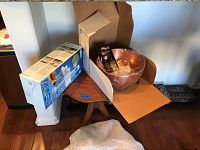 Full view of the lot showing the Braun blender box, a Revere Ware copper bowl in plastic wrap inside an open box, placed on a wooden table.