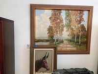 Two framed paintings on a wall above cabinets showing the landscape and donkey art.