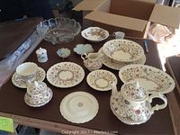 Full set laid out on table showing different pieces: dinner plates, salad plates, cup and saucer, sugar and creamer, teapot, vintage glass bowl and small dishes.