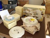 Photo of several Lenox boxes, cup and saucer sets, and plates on a table; includes boxed tea set and loose plates and cups/saucers.