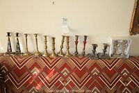 Photo of eleven candle sticks arranged on a patterned cloth, showing multiple sets of varying heights and styles.