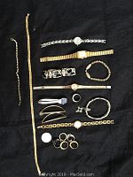 Costume jewelry assortment laid on black background including watches, bracelets, rings, and hair barrettes.