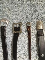 Close-up photo showing the sterling silver buckles and leather textures of the four belts laid side by side.