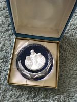 Crystal piece featuring relief of four faces in a cushioned box with satin interior.