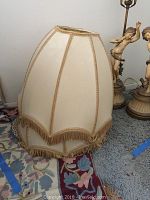 Close-up of two cream fabric lampshades, trimmed with beige fringe, positioned on the floor near the lamps