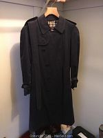 Black Burberry trench coat with belt and epaulets hanging in closet