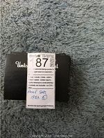 Black boxes containing 1982 US Mint Proof Sets stacked on a light blue carpet, showing original packaging with a MaxSold sticker detailing lot number 87P and condition.