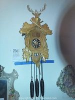Full frontal view of cuckoo clock showing carved deer head, rifles, oak leaves, chains and three weights