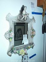 Porcelain cherub wall mirror mounted on wall, showing cherub figure and floral detailing