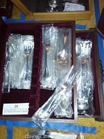 Full view of flatware pieces, each sealed in original plastic, arranged in original dark wood non-tarnish box with burgundy velvet lining.