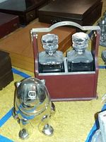 Both items displayed together on carpet: bear shaker at front, leather-covered wood carrier with brass handle and two glass decanters behind